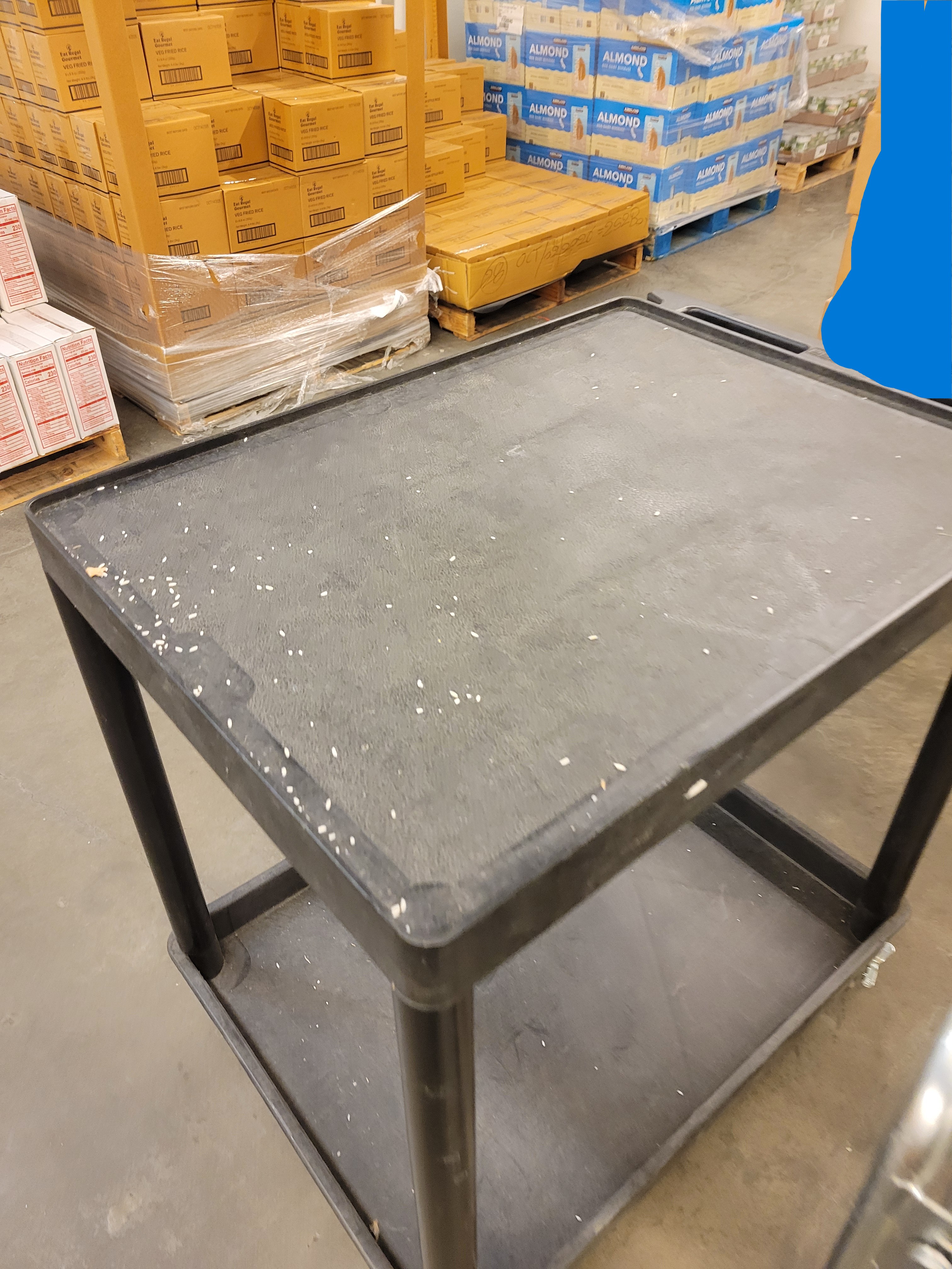 Shelf cart with tiny rice spilled on top of it in a room full of pallets.